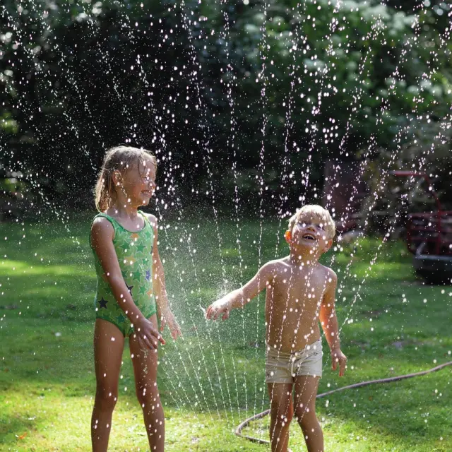To børn leger med en vandspreder i haven